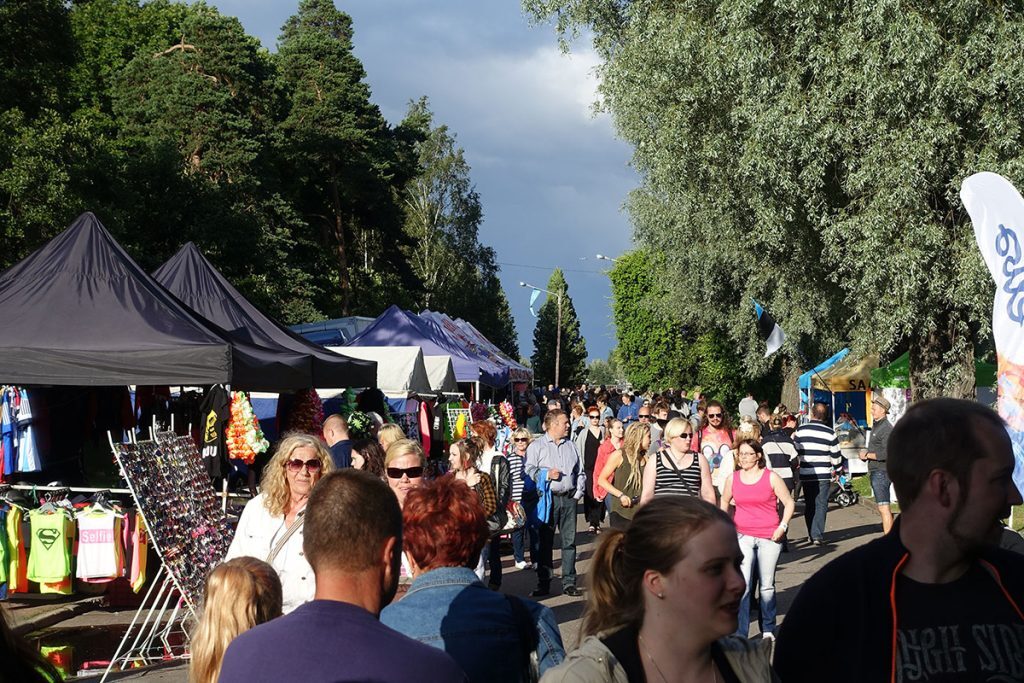 Ihmisiä kuljeskelemassa markkinakadulla. Markkinatelttoja vasemmalla, väkijoukko oikealla.