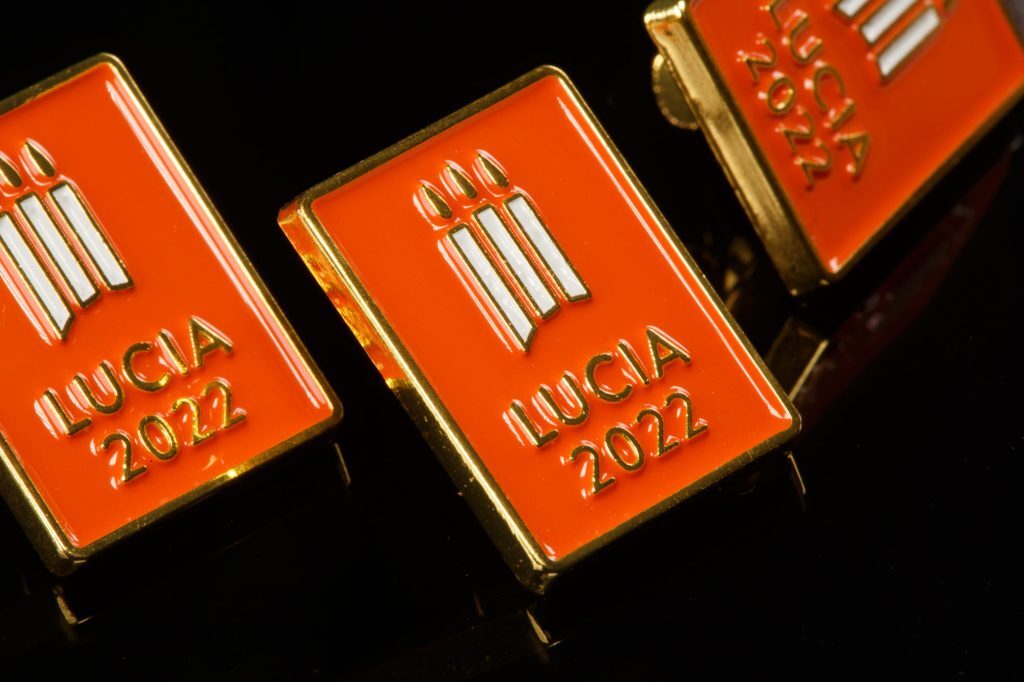 Vuoden 2022 Lucia-merkkejä. Punainen suorakulmainen pinssi, jossa on kolme kynttilää ja teksti LUCIA 2022.