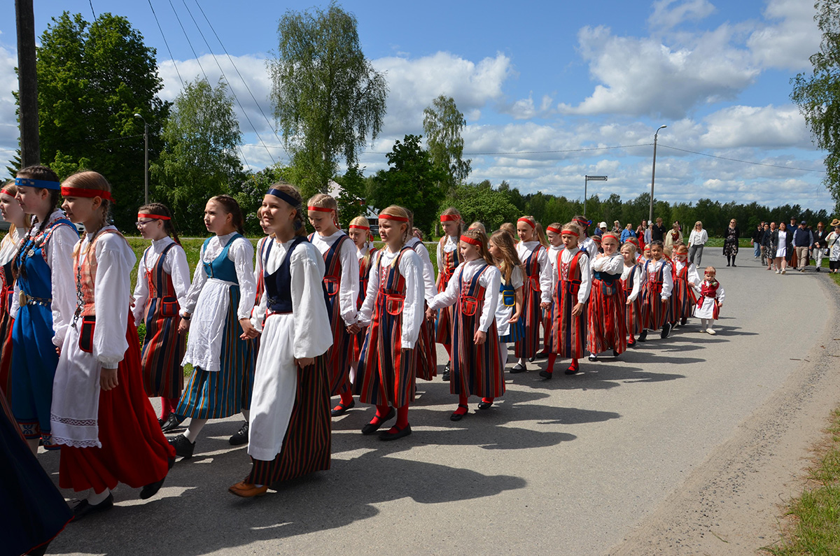 Neitojen kulkue Ritvalan helkajuhlilla 2025. Kansallispukuisia nuoria naisia kävelemässä tietä pitkin kuvassa vasemmalle.